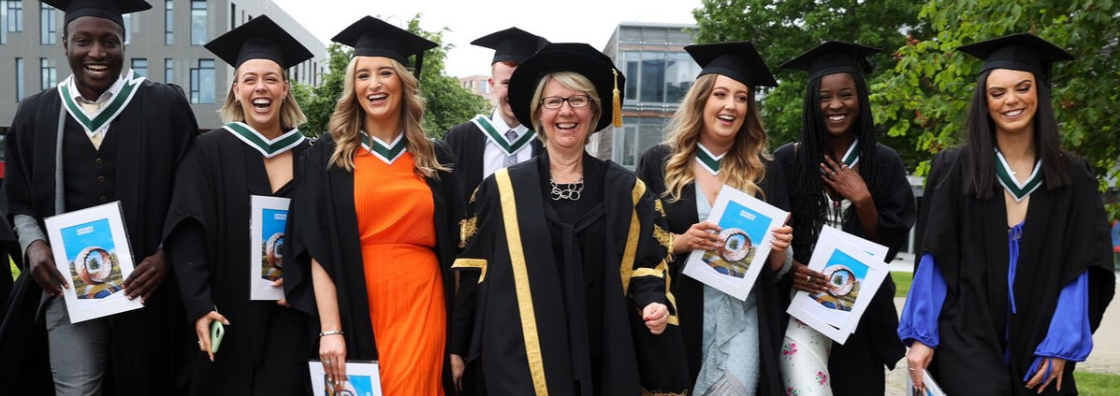 Image of smilling university president with a group of students in graduation gowns