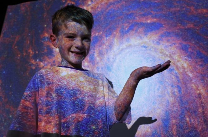 young child holding hand up in front of a multicoloured space backdrop