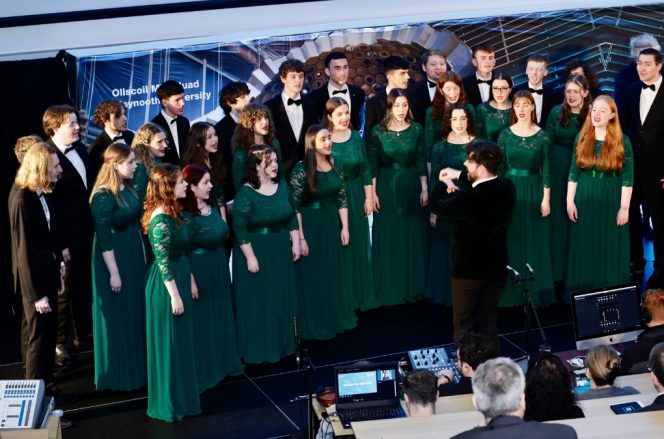 pictured are the maynooth university choir, a line of females at the front wearing  green dresses and males wearing tuxedo