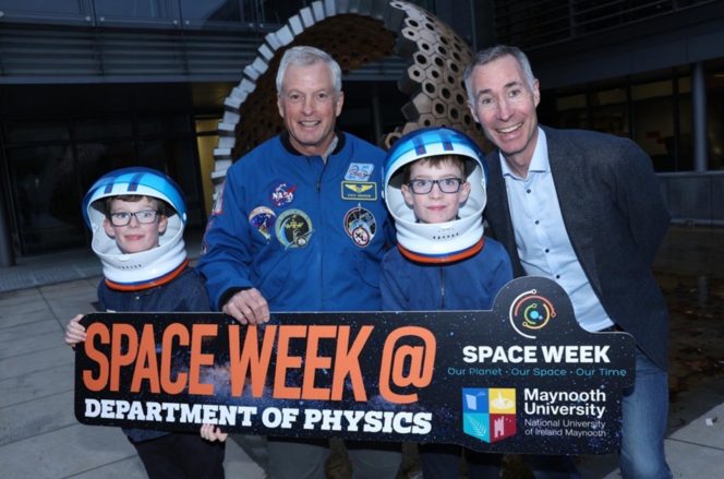 2 children in space helmets with two gentleman, holding an event sign called Spaceweek, blue