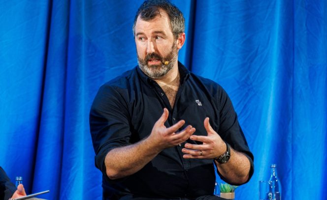 Man in navy blue shirt with hand raises discussion topic as part of panel discussion