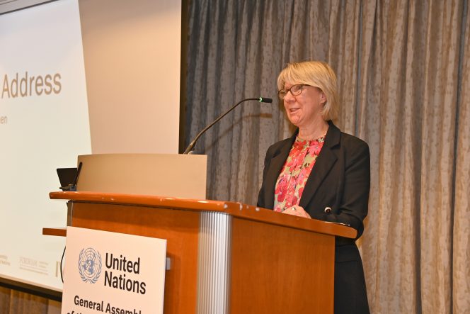 Woman in a black jacket and red blouse standing behind a lectern