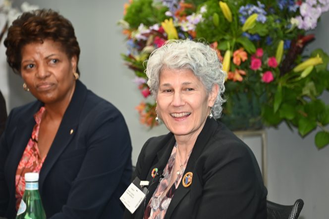 Two women in black suits with flowers behind them