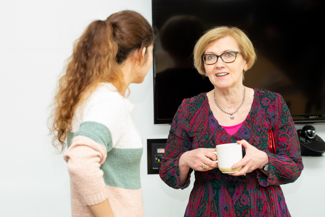 2 ladies speaking one with her back to the camera on facing the camera holding a mug