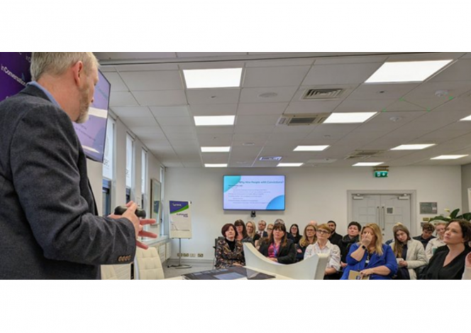 Joe Garrihy speaks to a group of people in a white room