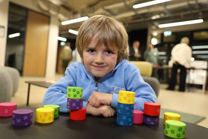 Young boy in a blue jumper sits at a table with coloured blocks