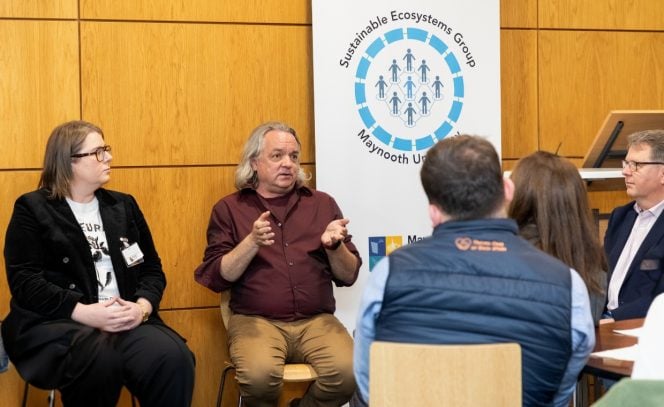 1 man and 1 woman, part of panel discussion with pull up banner and text Sustainability Ecosystems Group Maynooth University, wine, beige, black, white