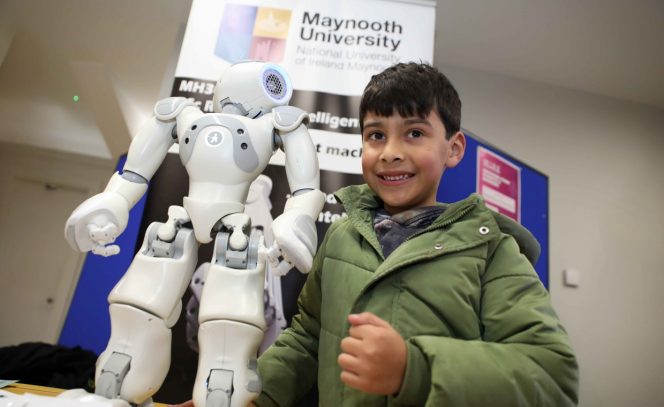 Boy in a green jacket poses with a robot