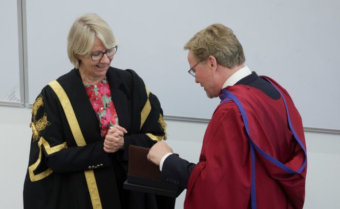 woman presenting award to man, black robe, wine robe, glasses