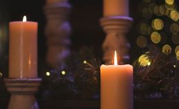 Lit candles against a soft, dark background of pine branches and twinkly lights