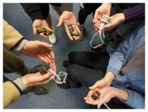 5 peoples hands in a circle holding technological devices