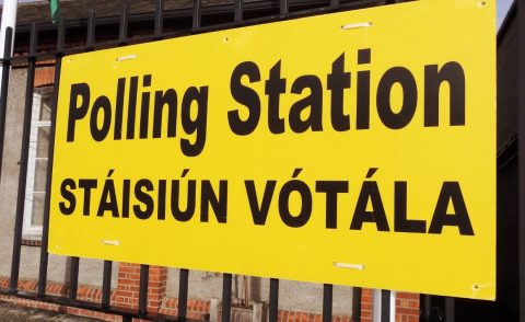 Large yellow sign hanging on railings outside a building that reads: Polling station/Stáisiún Vótála