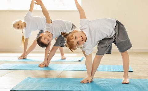 Three children -- two girls and a boy -- standing on blue yoga mats doing triangle poses