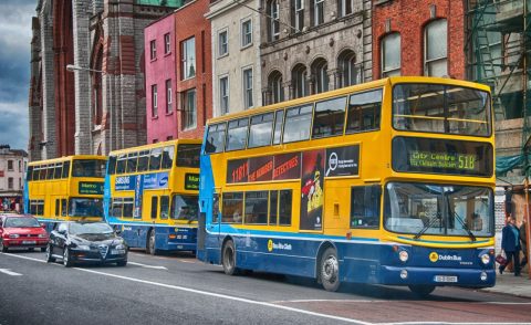 Three Dublin buses lined up on the street with cars passing by