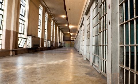 Prison corridor with row of cells separated from a row of windows by orange-floored walkway