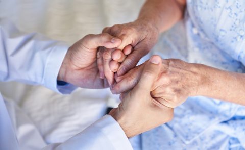 Hands of a man in a blue shirt holding those of an older woman in a blue dress