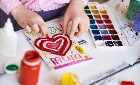 Child's hands making a card with a love heart that says 'I love you, Mum'