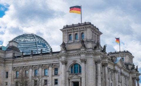 Ornate grey building with a glass dome and a German flag flying from the tower