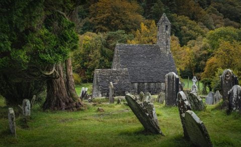 Small stone church with trees behind it and grave stones in front of it