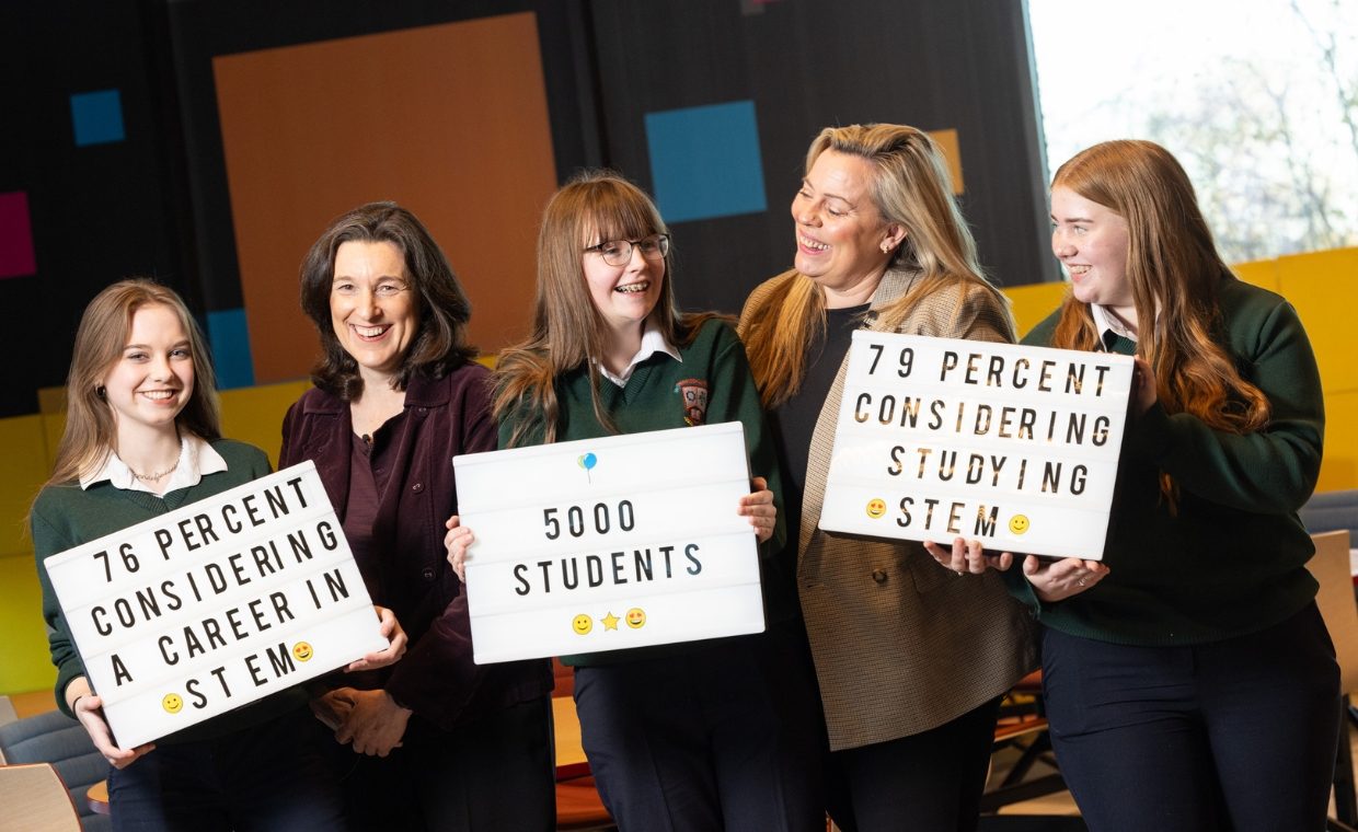 3 young girls in school uniform, and 2 mature women smiling, and holding signs that state '76 percent considering a career in stem', '5000 students' and '79 percent considering studying STEM' 