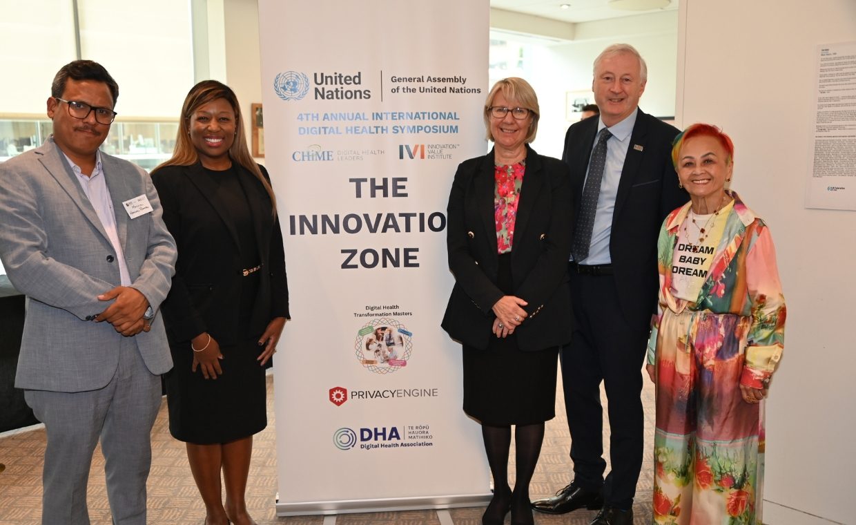 Man in a grey suit, woman in a black suit standing to the left of a banner that reads The Innovation Zone with a woman in a black suit and red blouse, a man in a black suit and a woman in a colourful outfit standing to the right