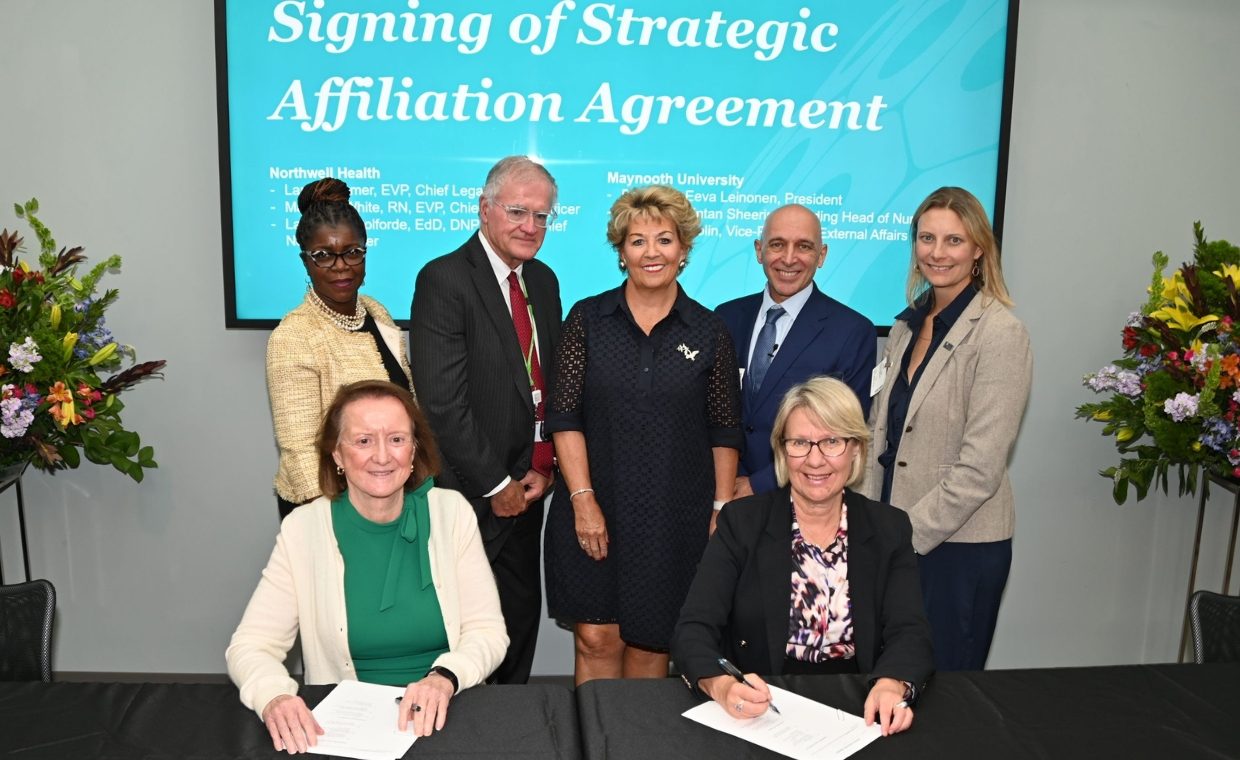 Five people standing and two women sitting in front of a turquoise banner