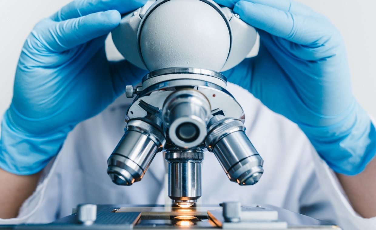 Person wearing blue gloves viewing a microscope