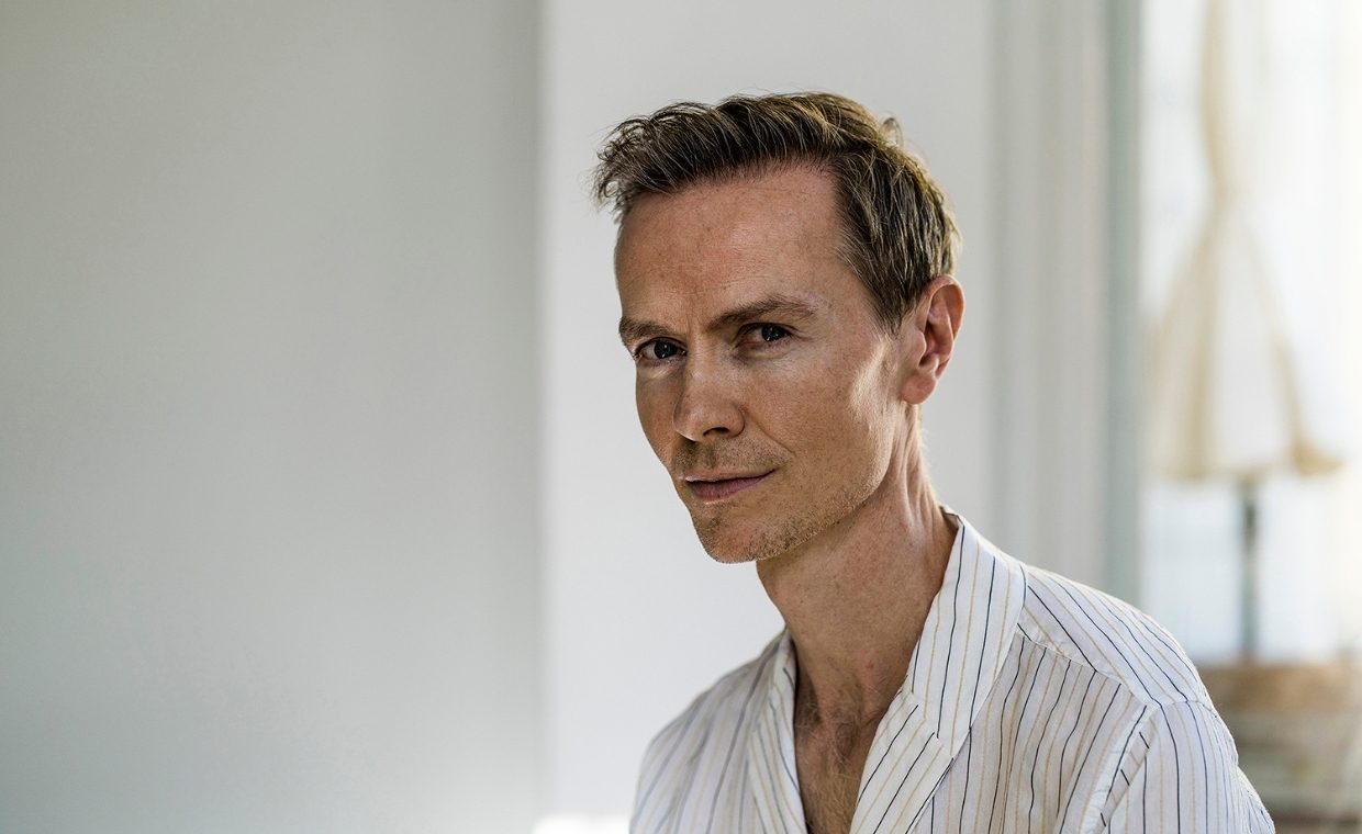 Pensive man in an open-necked white shirt with window in the background