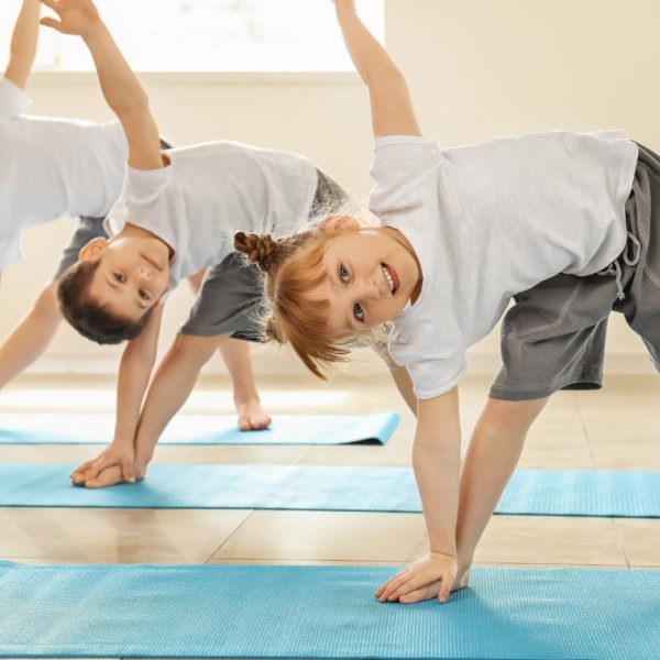 Three children -- two girls and a boy -- standing on blue yoga mats doing triangle poses