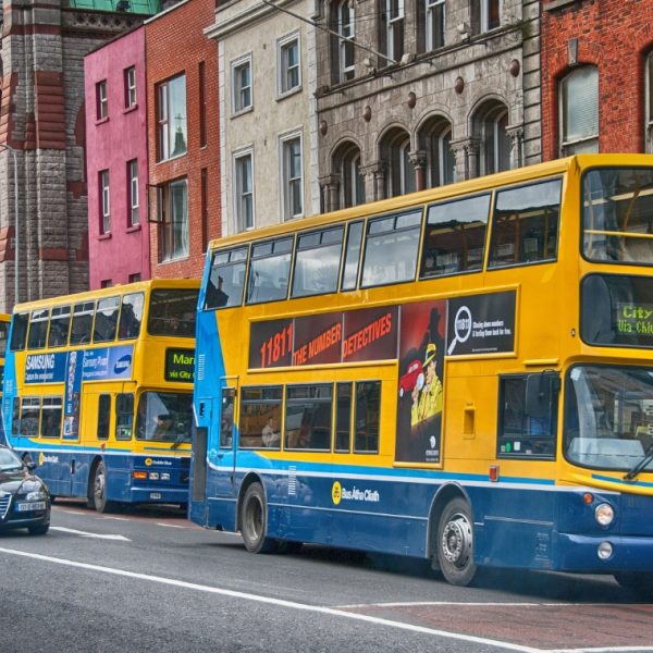 Three Dublin buses lined up on the street with cars passing by