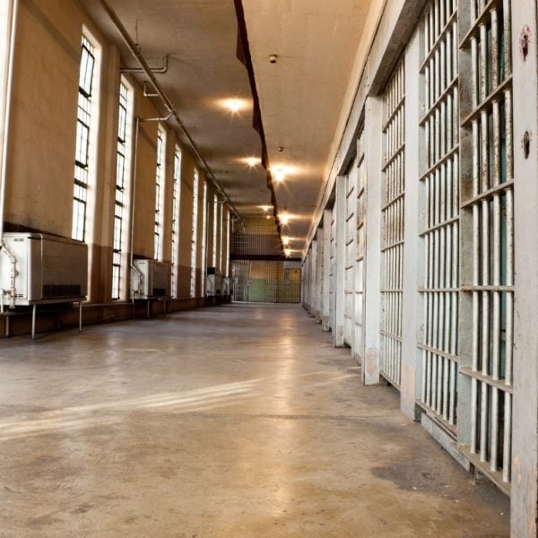 Prison corridor with row of cells separated from a row of windows by orange-floored walkway