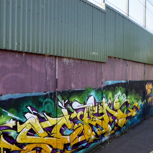 Wall with grafitti on the bottom topped by a high fence