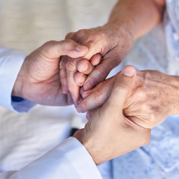 Hands of a man in a blue shirt holding those of an older woman in a blue dress