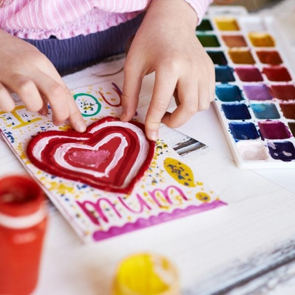 Child's hands making a card with a love heart that says 'I love you, Mum'