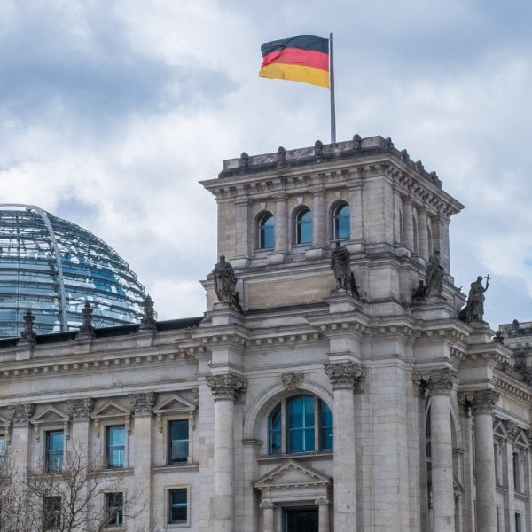 Ornate grey building with a glass dome and a German flag flying from the tower