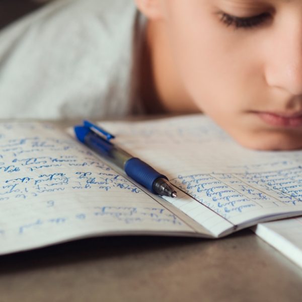 Child with sad face and head resting on table. Book with writing and a pen