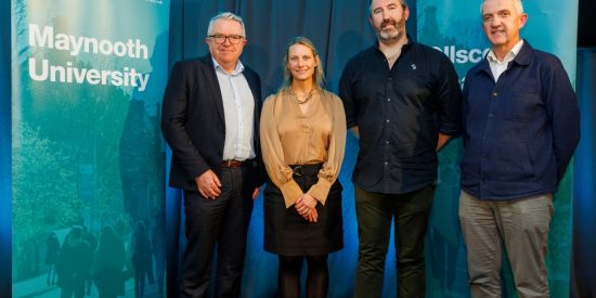 3 men and 1 woman posing for photographer - black, navy, blue, tan colours appear on clothing