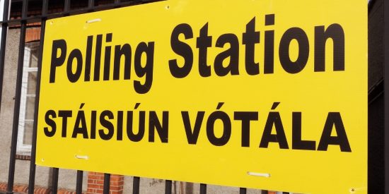 Large yellow sign hanging on railings outside a building that reads: Polling station/Stáisiún Vótála