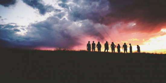 A group of people stand in silhouette against sunrise