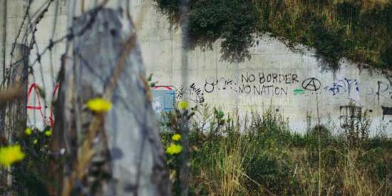 A picture of a wall in an area of wasteland with 'No Borders' spraypainted on it