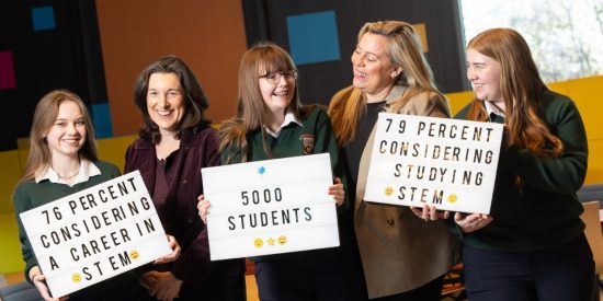 3 young girls in school uniform, and 2 mature women smiling, and holding signs that state '76 percent considering a career in stem', '5000 students' and '79 percent considering studying STEM' 