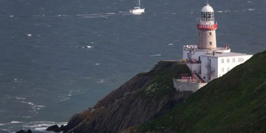 White and red lighthouse building sitting on a rocky outcrop with a boat approaching by sea