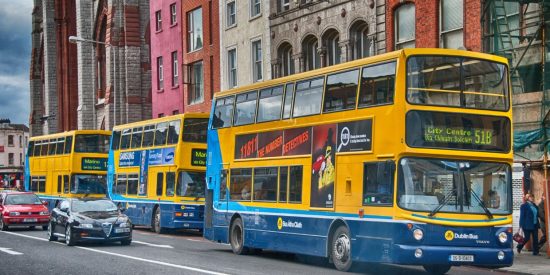 Three Dublin buses lined up on the street with cars passing by