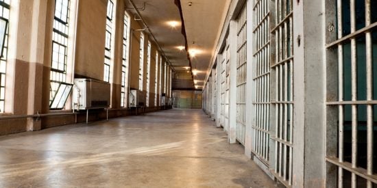 Prison corridor with row of cells separated from a row of windows by orange-floored walkway