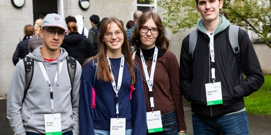 Male student in grey jumper with baseball cap, female student in navy jumper, female student in brown jumper and male student in black jacket