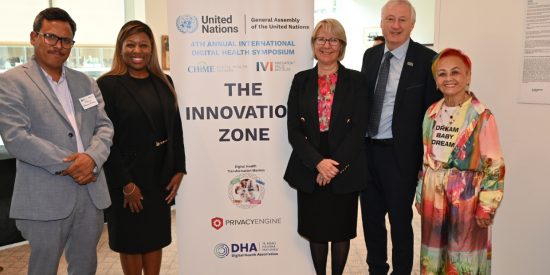 Man in a grey suit, woman in a black suit standing to the left of a banner that reads The Innovation Zone with a woman in a black suit and red blouse, a man in a black suit and a woman in a colourful outfit standing to the right