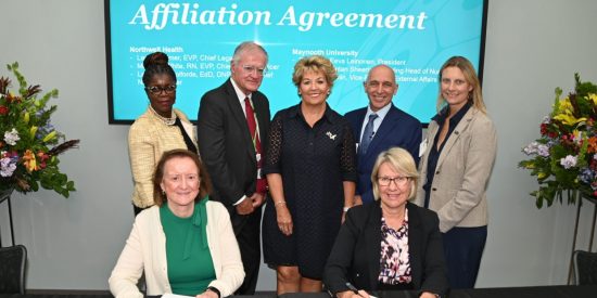 Five people standing and two women sitting in front of a turquoise banner