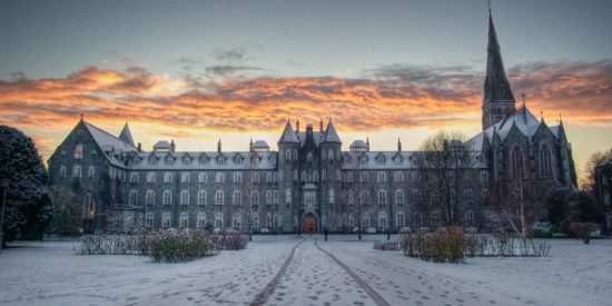 large old style building with a church steeple. Sun is setting and snow is present in the image