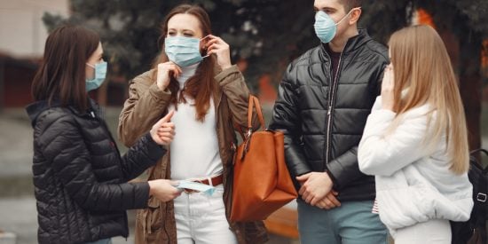 3 women and 1 man talking to each other wearing covid masks. Black jackets. blue jeans, white jacket and brown jacket 