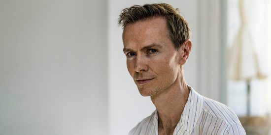 Pensive man in an open-necked white shirt with window in the background